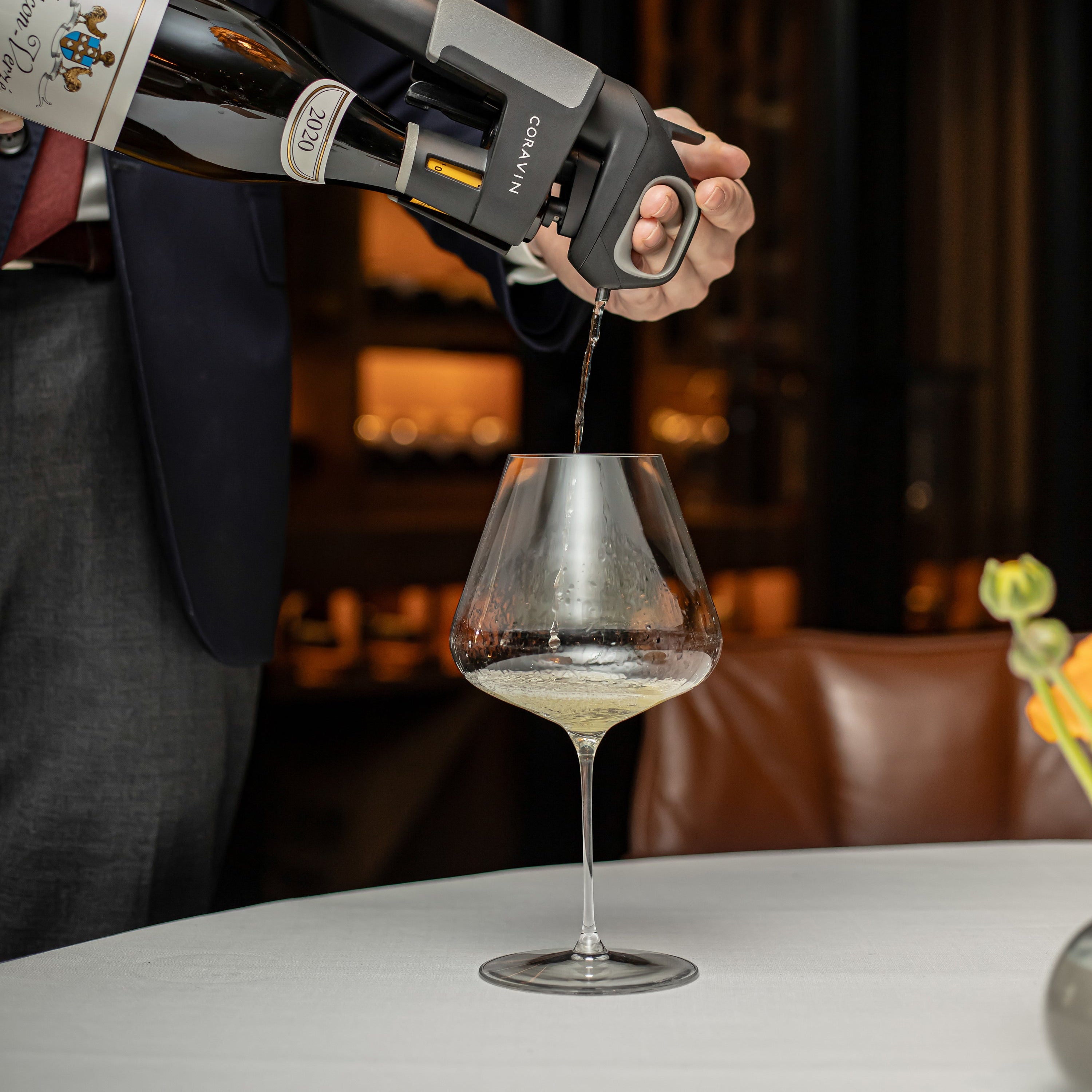 A Coravin Timeless system pours white wine into a wide glass at a fine dining table with elegant ambiance.