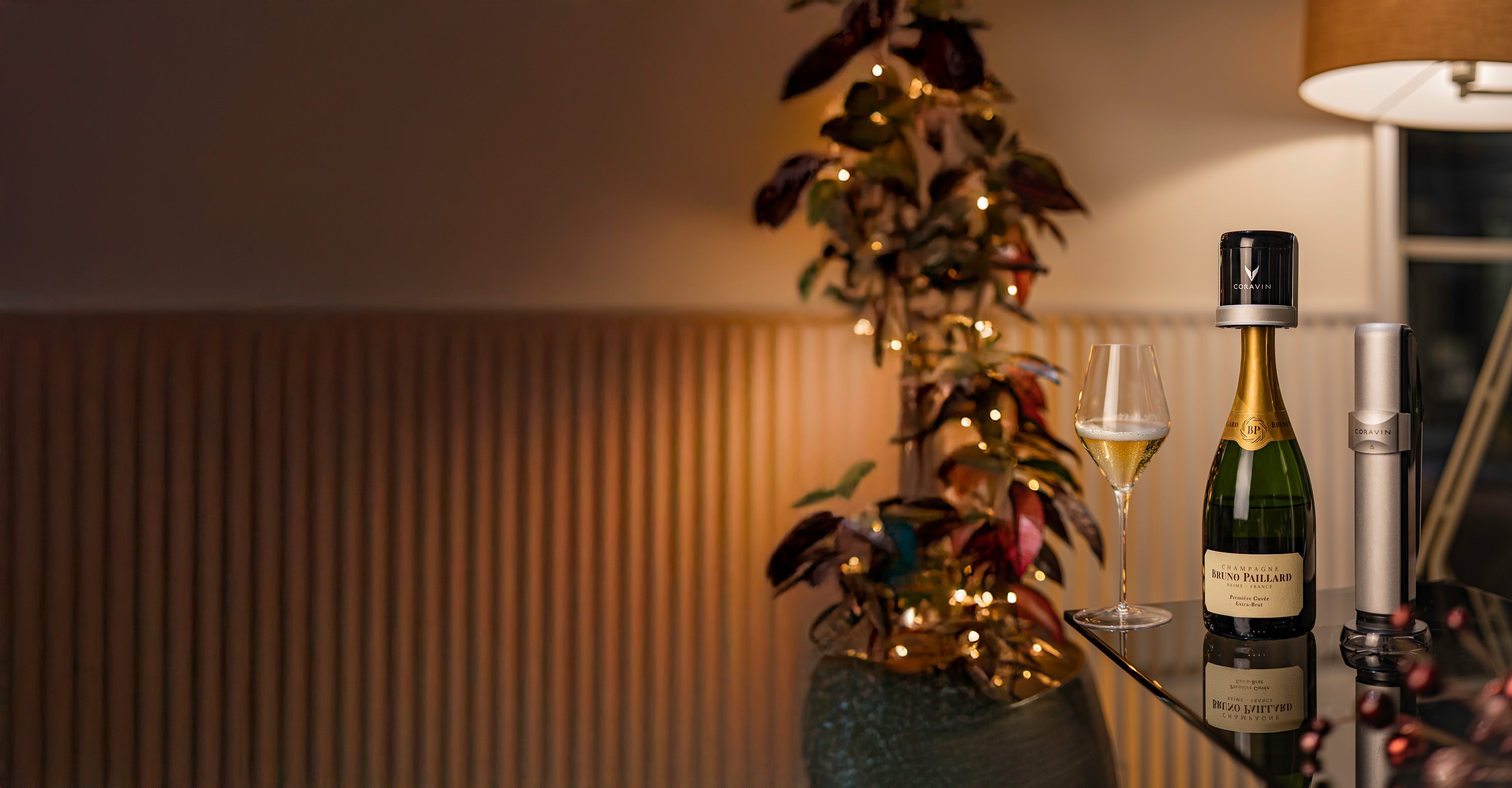 Bottle of champagne and a glass on a table with decorative plants and warm lighting.