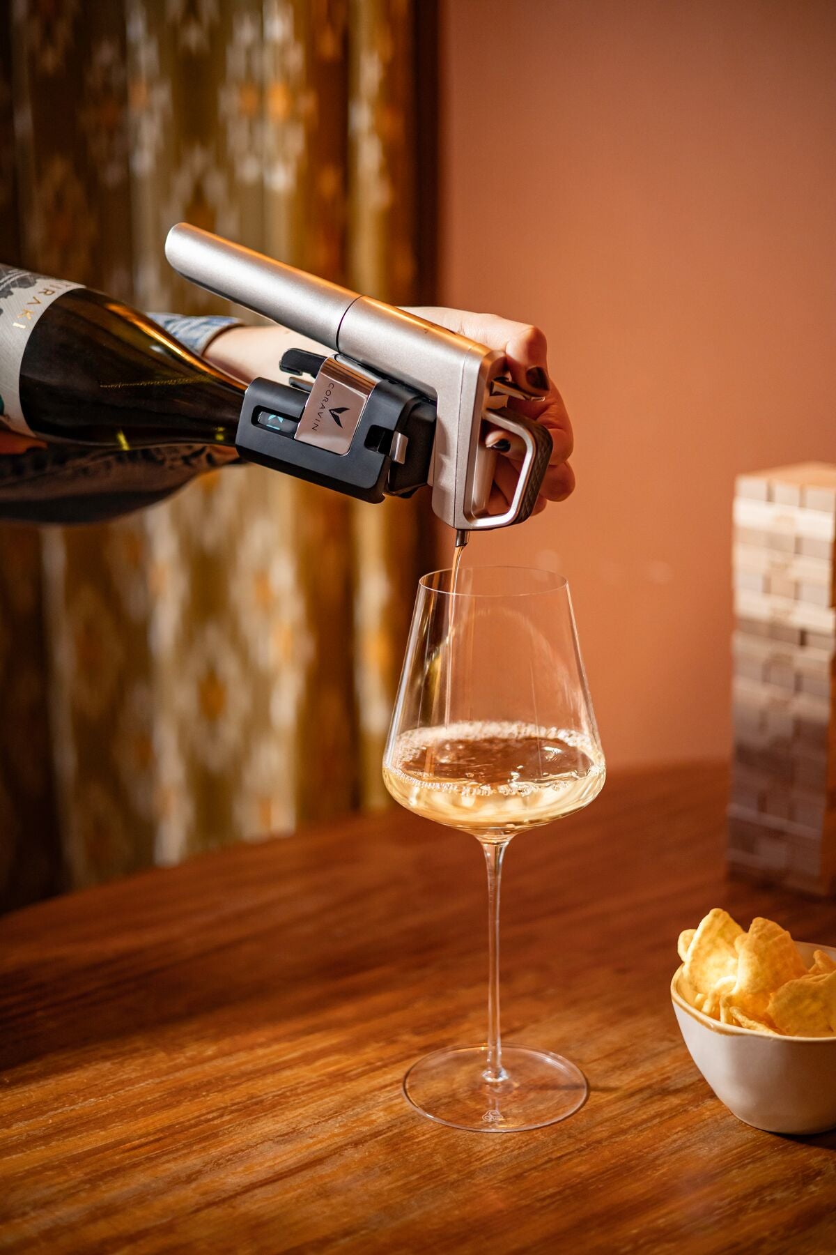 Person opening a bottle of wine with a coravin timeless pouring it into a glass on a wooden table with chips.